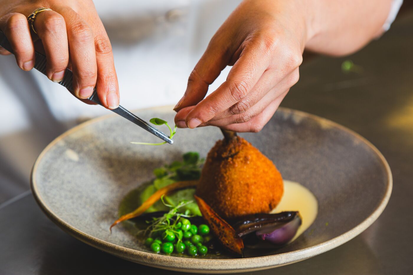 Chef's hands meticulously garnish a gourmet dish with green herbs.