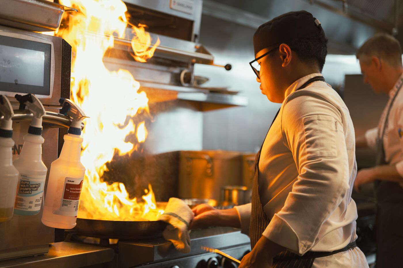 A chef performs a spectacular flambé in a professional kitchen, creating a visual spectacle with fire and culinary skill.