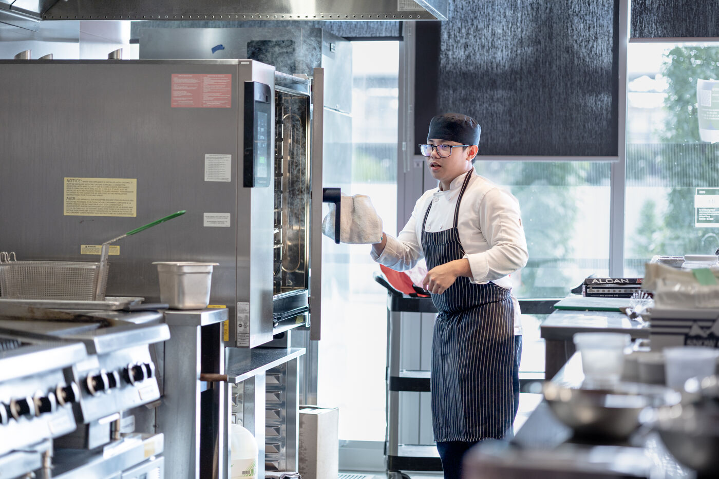 A chef is meticulously cleaning a large industrial oven in a professional kitchen setting, ensuring everything is spotless before service begins.