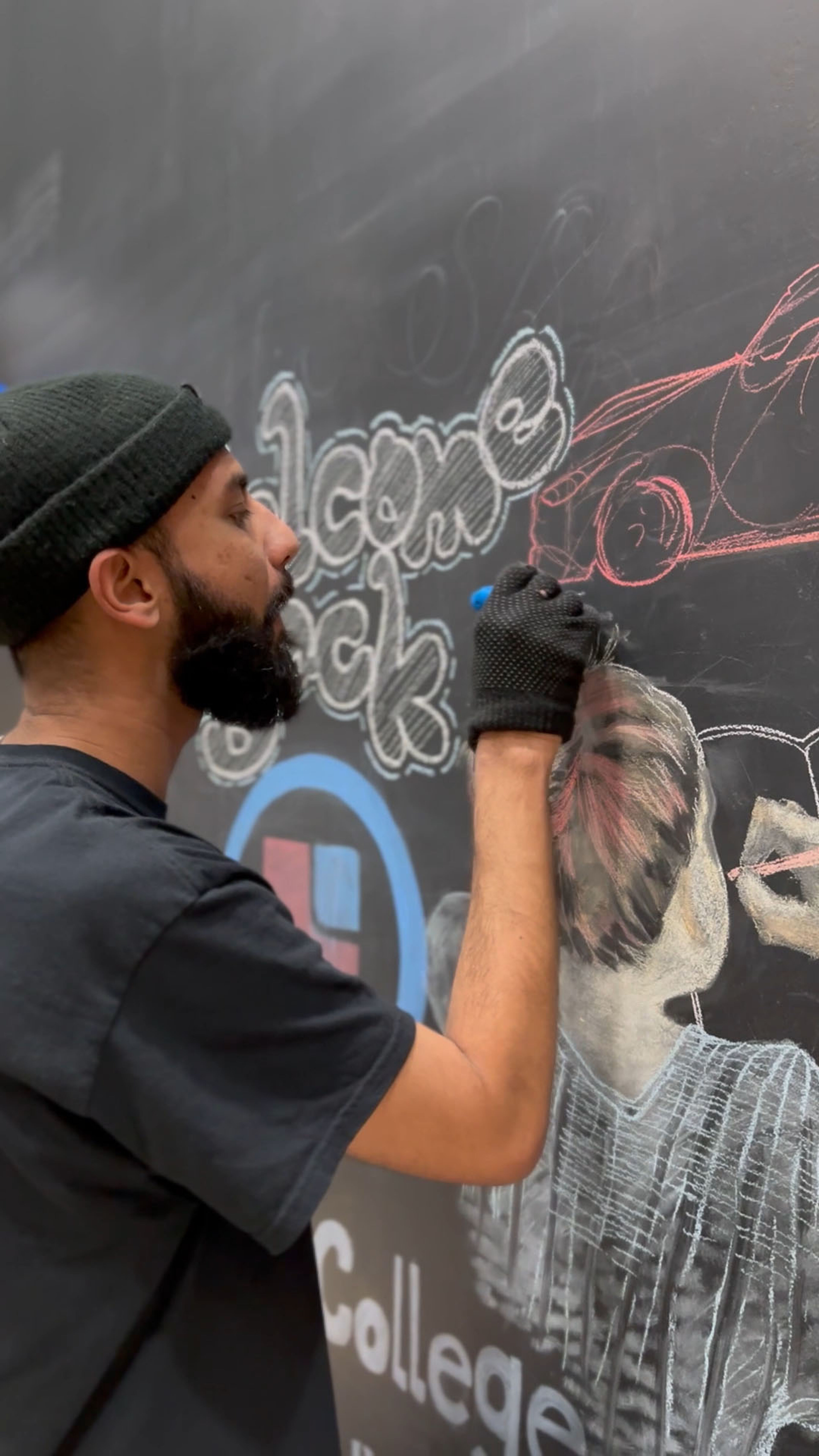 A focused male artist sketches on a chalkboard, detailing a human portrait with white chalk, surrounded by colorful chalk text.