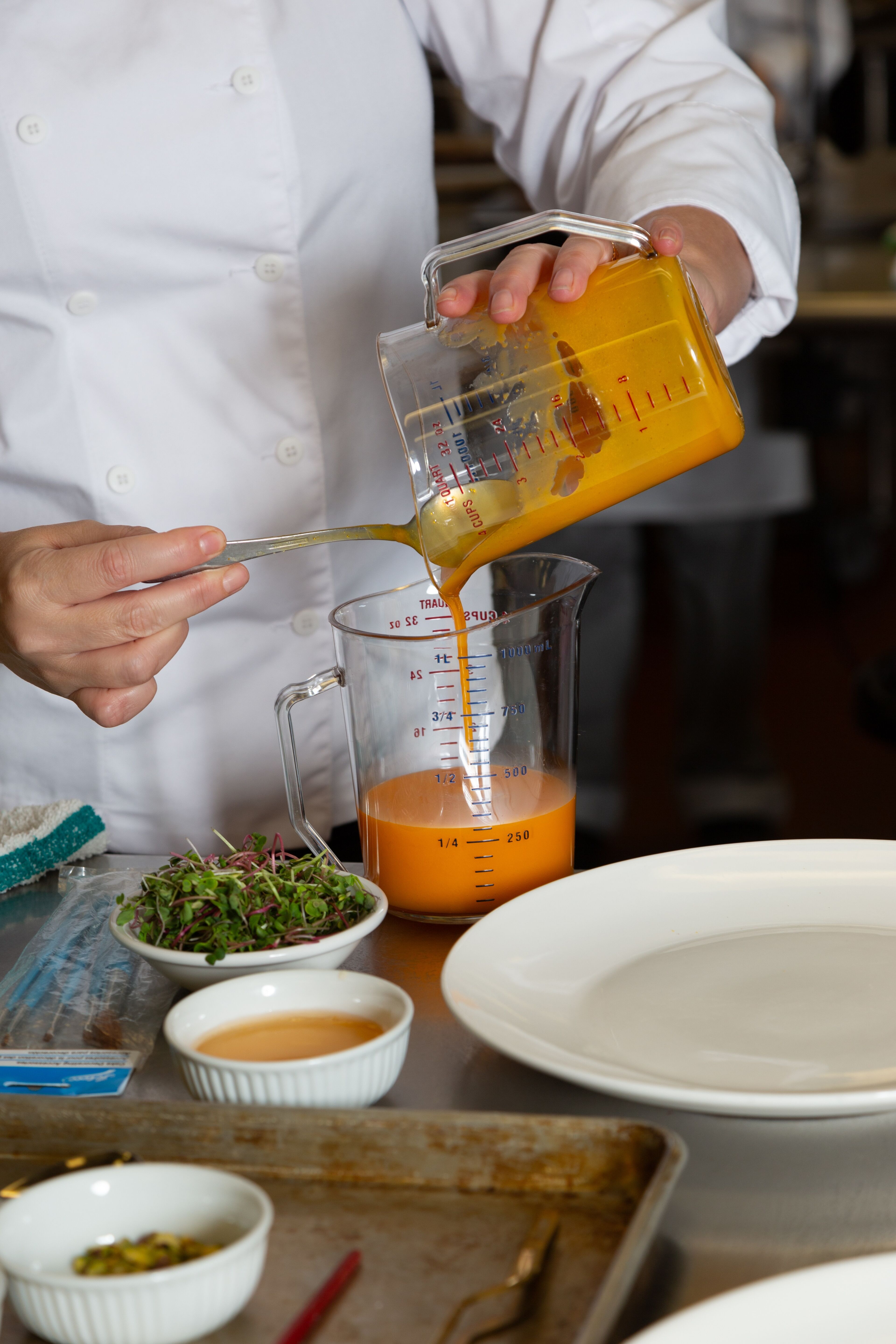 A chef transfers a bright orange sauce from one measuring jug to another, with precision and care.