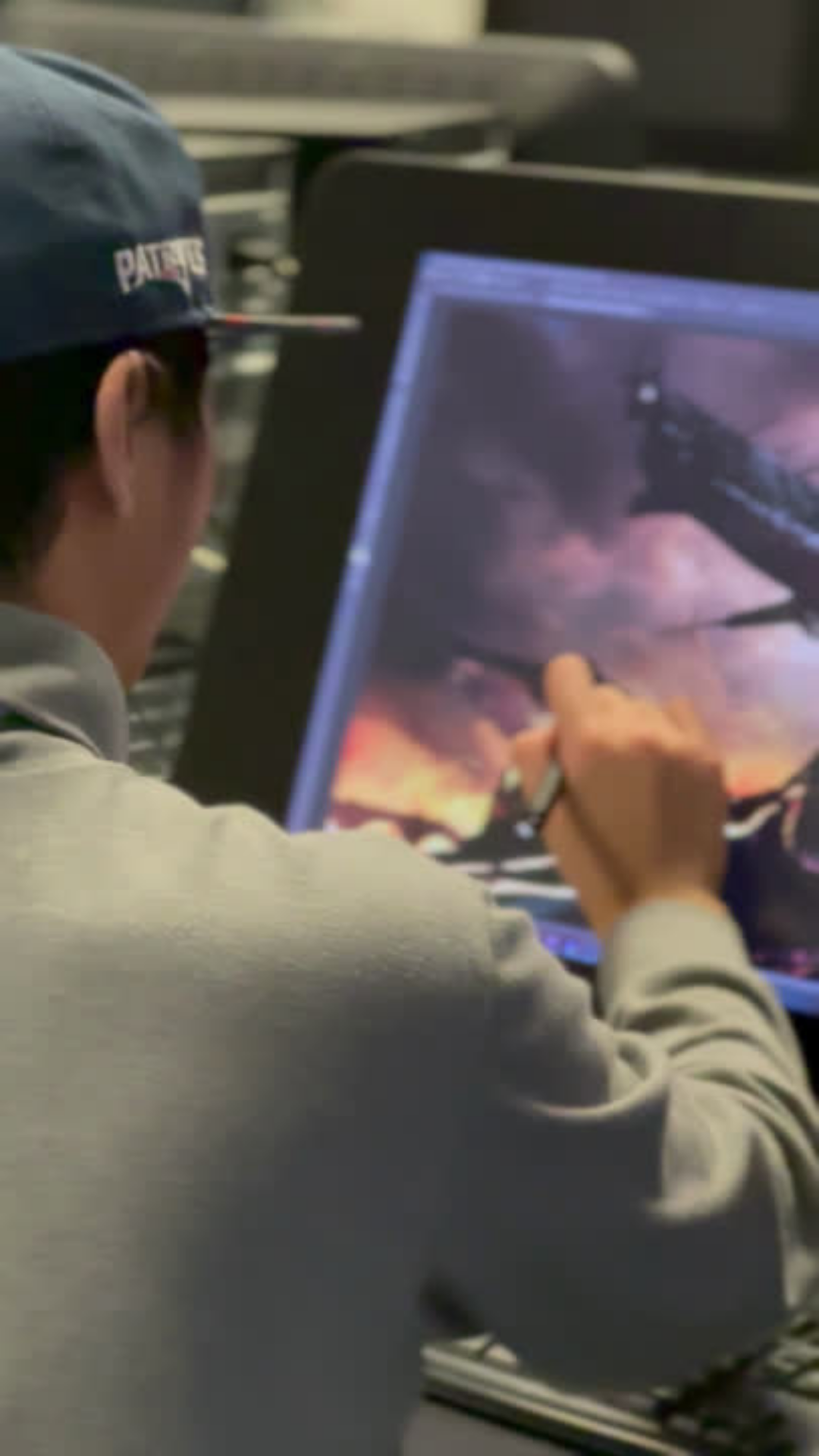 An individual in a baseball cap is focused on creating art on a digital tablet, which displays a colorful, fiery scene.
