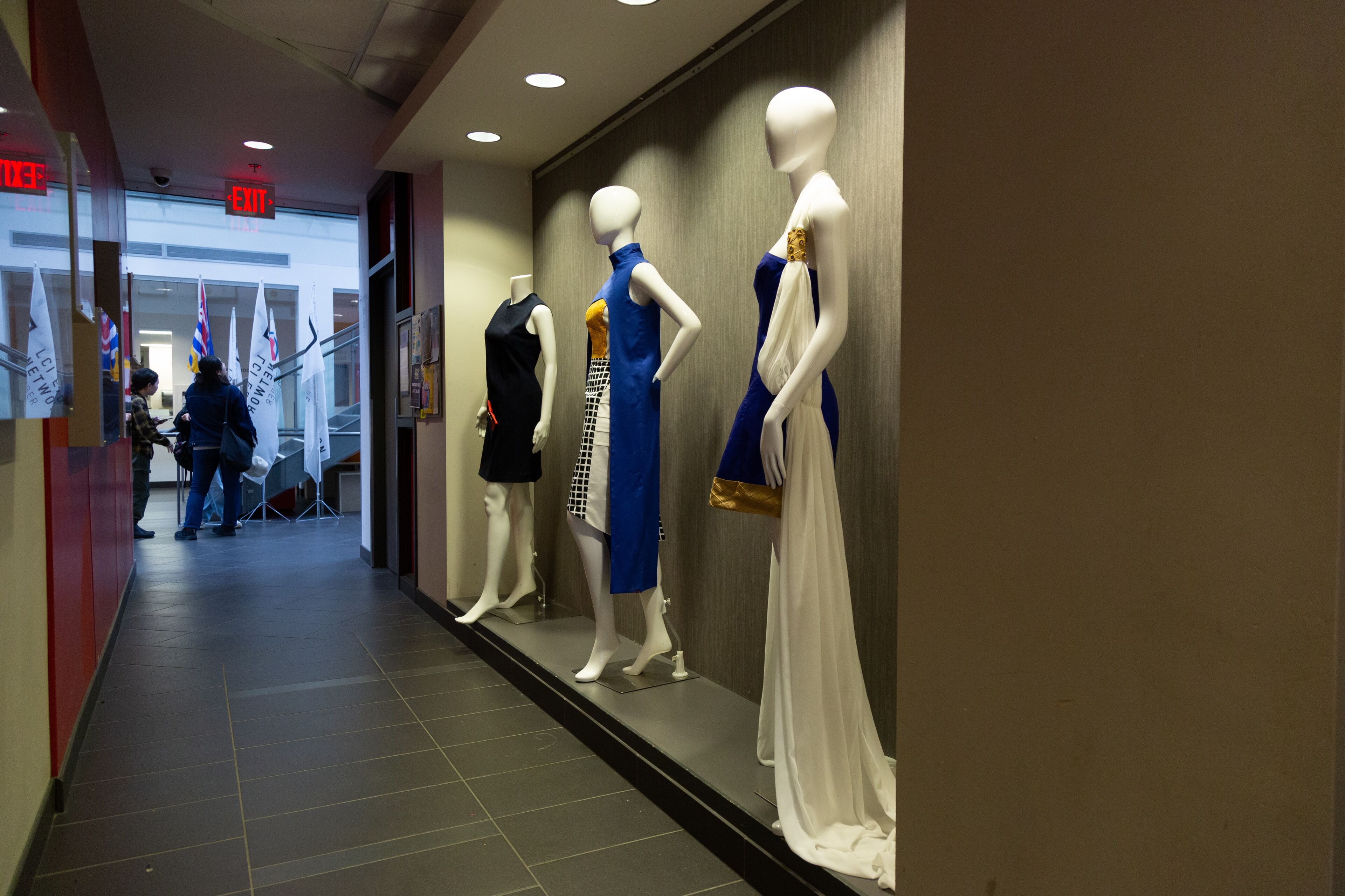 A lineup of mannequins presenting evening dresses as part of a fashion exhibition in a college corridor.