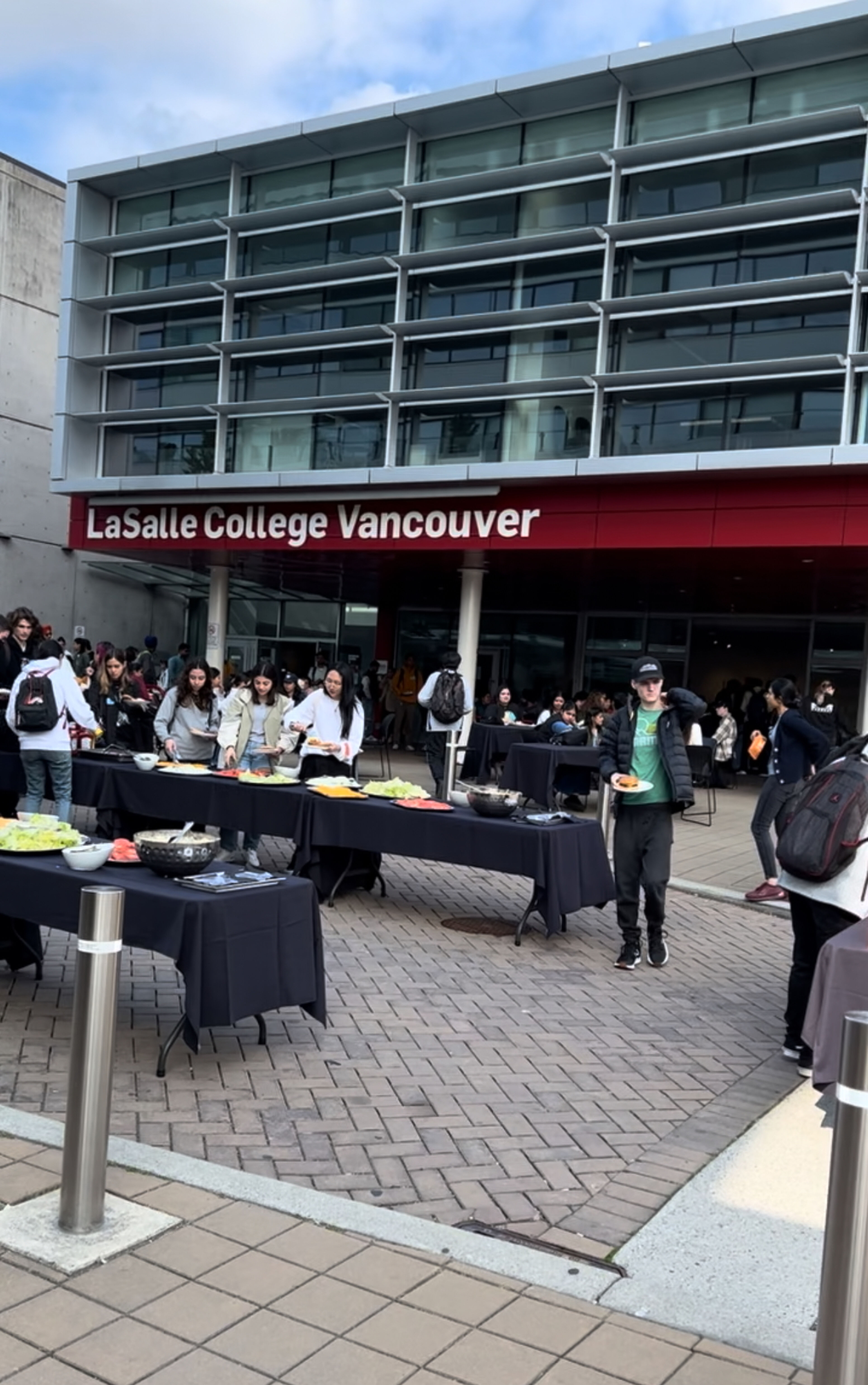 Students gather for an event outside LaSalle College Vancouver, with food served at multiple tables under an overcast sky.