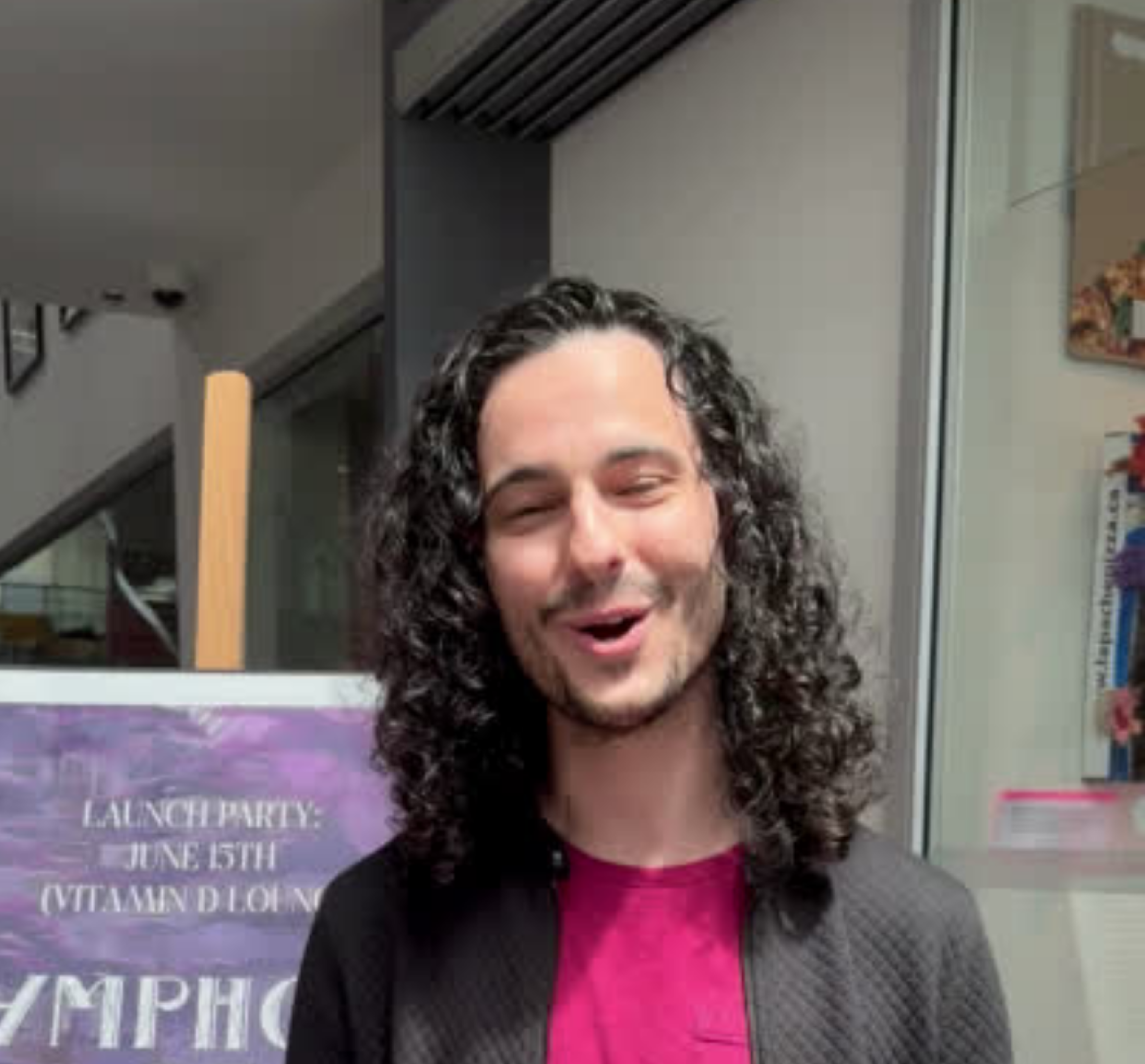 A cheerful man with long curly hair presenting a signboard for a launch party event.